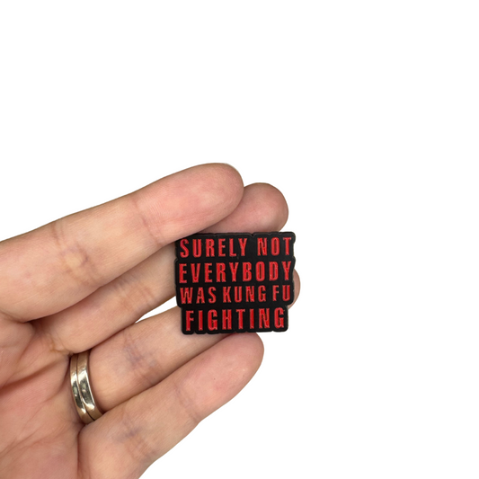 Person holding enamel pin that says “Surely not everybody was kung fu fighting”