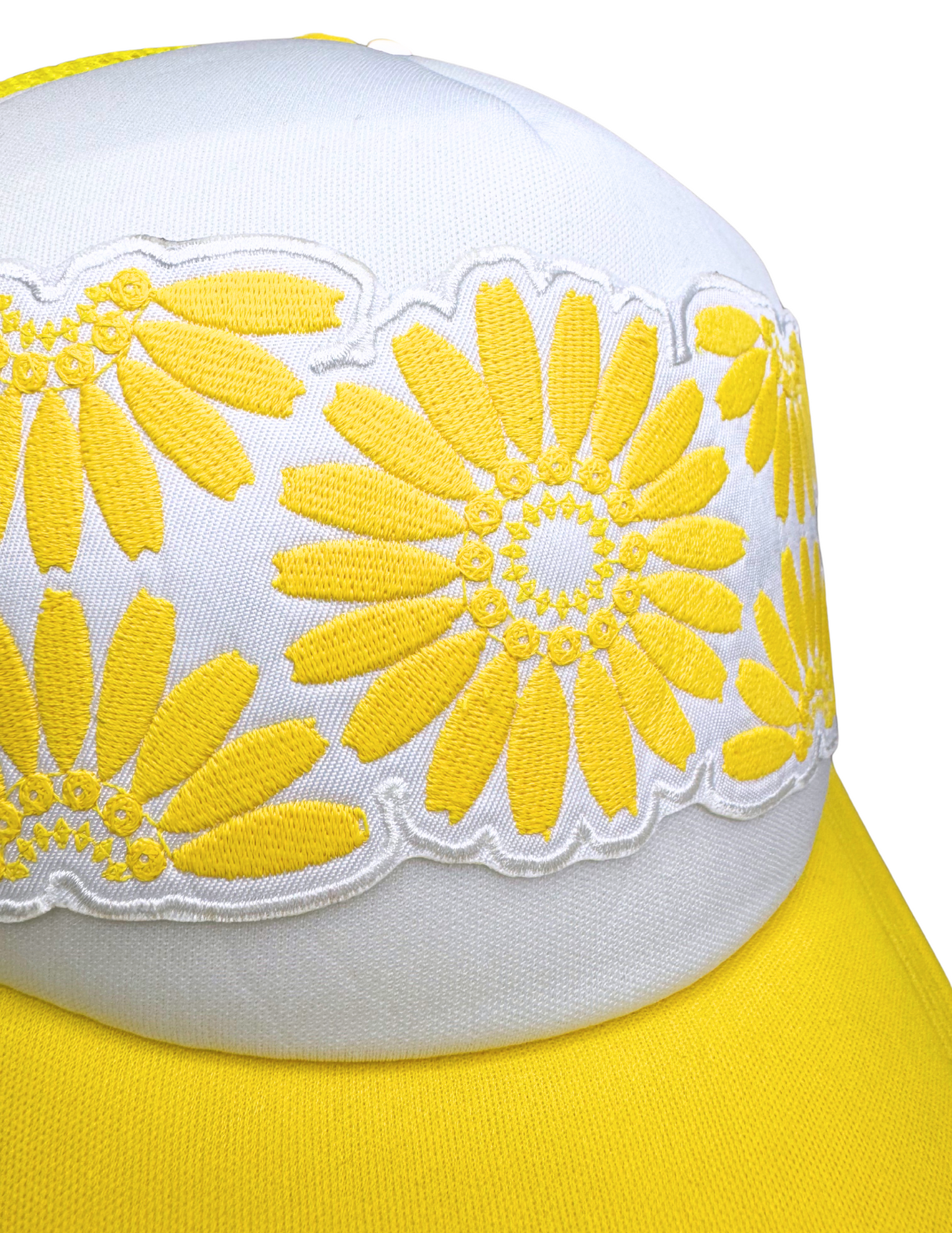 Closeup of sunny yellow daisy embroidery on white foam trucker hat, referencing vintage Pyrex design