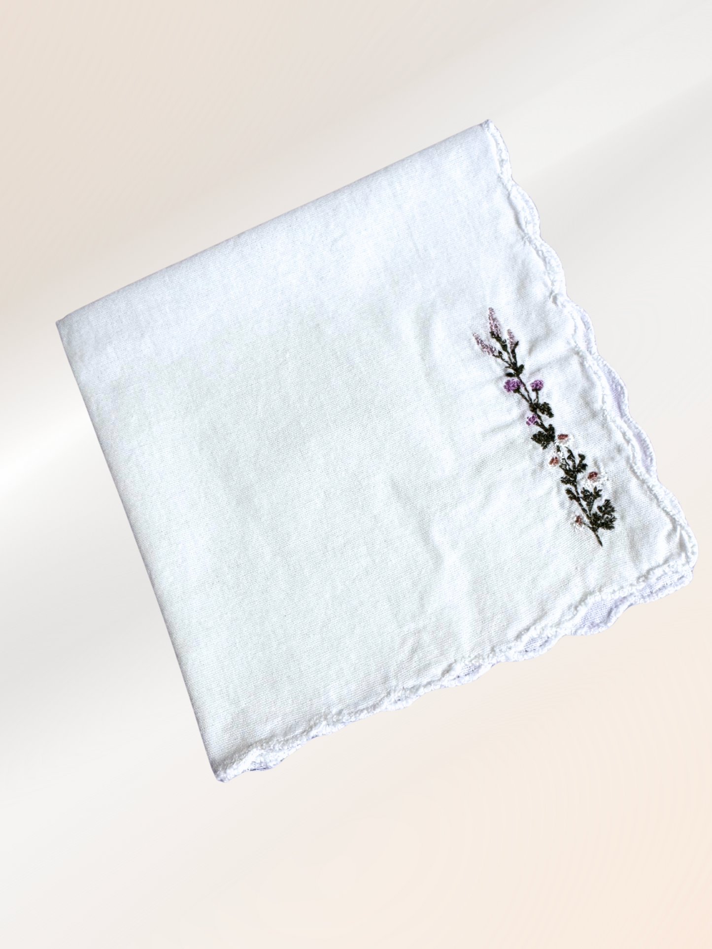 A folded embroidered handkerchief showcasing a delicate lavender vine stitched in purple and green on soft white fabric, handmade in Kansas City.