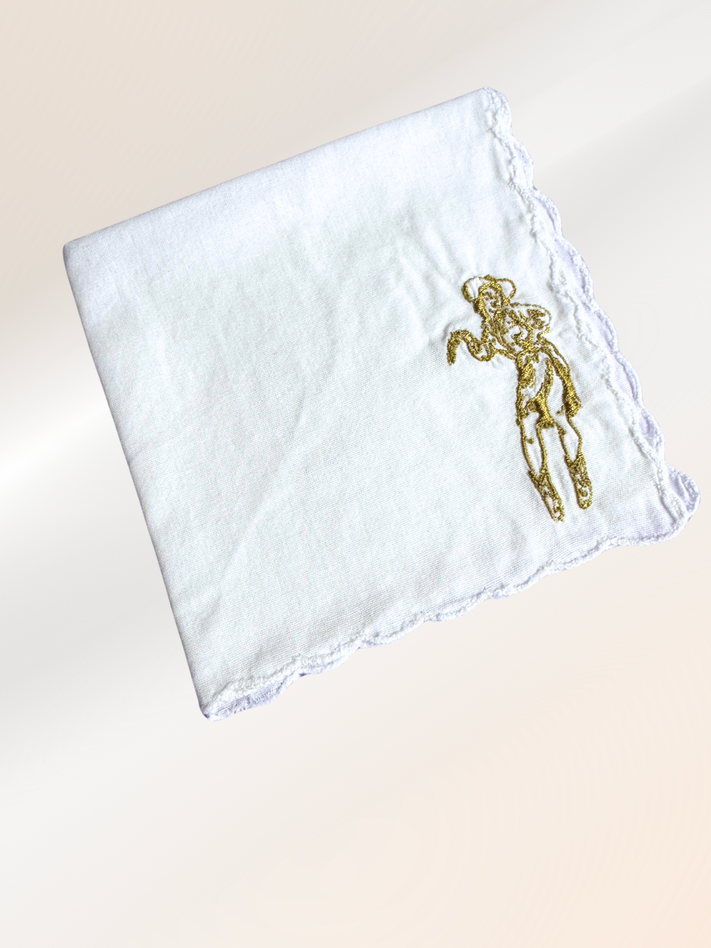 A folded embroidered handkerchief showcasing a retro Western cowgirl stitched in gold on soft white fabric, handmade in Kansas City.