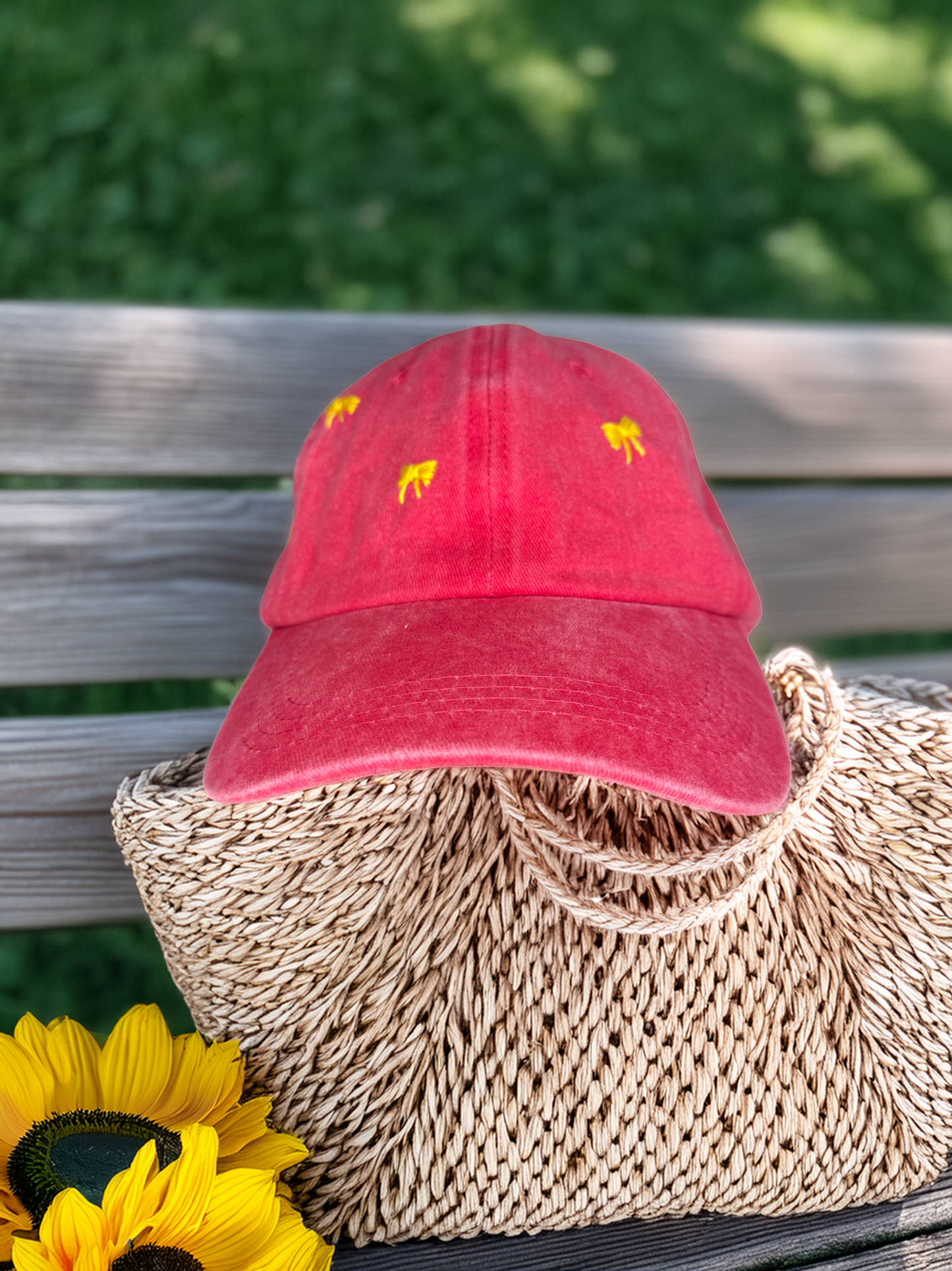 Red cap with yellow designs on a woven bag with sunflowers, against a blurred green background