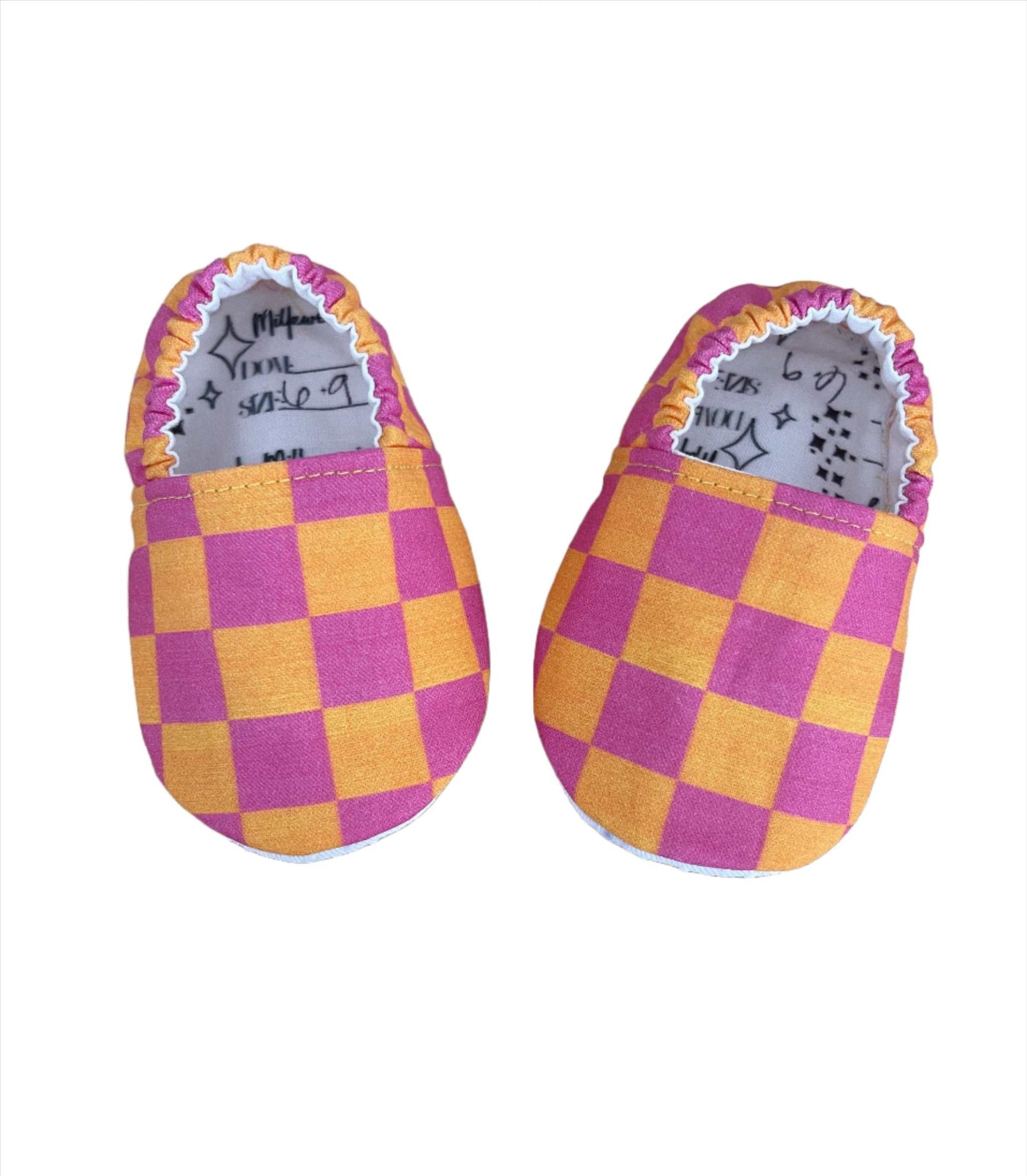 Neon pink and orange checkerboard moccasins for babies, soft fabric, stylish design.
