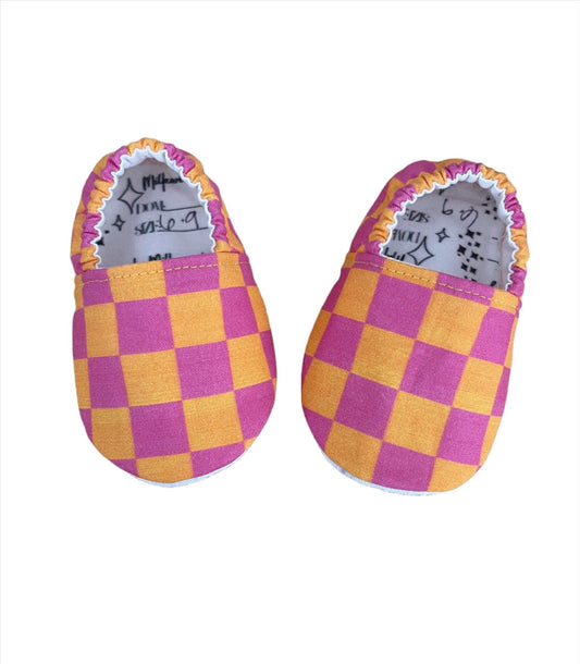 Neon pink and orange checkerboard moccasins for babies, soft fabric, stylish design.