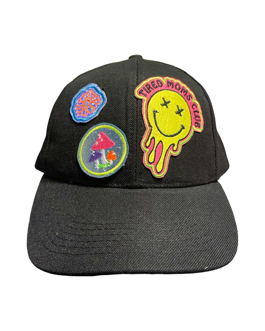 Black baseball hat with "Tired Moms Club" neon patches featuring holographic flower and glittery neon mushrooms.