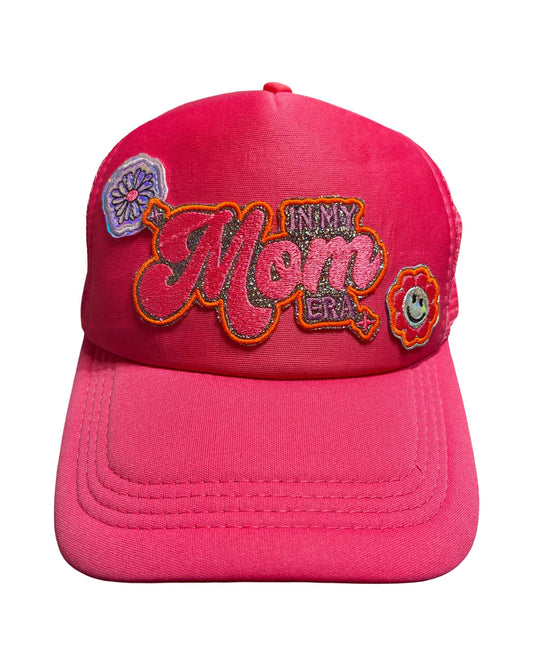 Hot pink trucker hat with 'In My Mom Era' patch and holographic flower accents.
