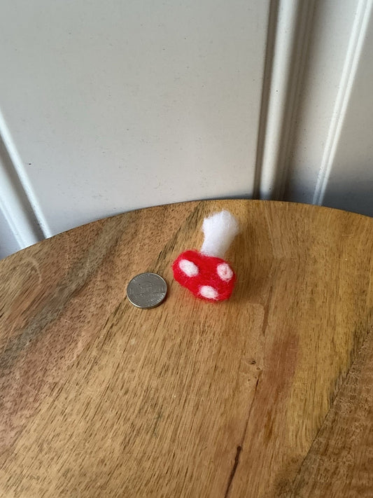 A small red and white mushroom-shaped object with a white fluffy top sits on a round wooden table next to a coin, with a white paneled wall in the background.