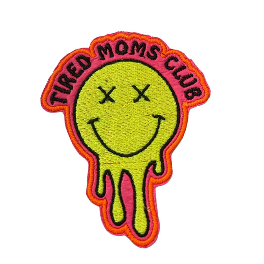 Handmade Tired Moms Club iron-on patch with neon pink vinyl, neon yellow smiley, and neon orange outline.