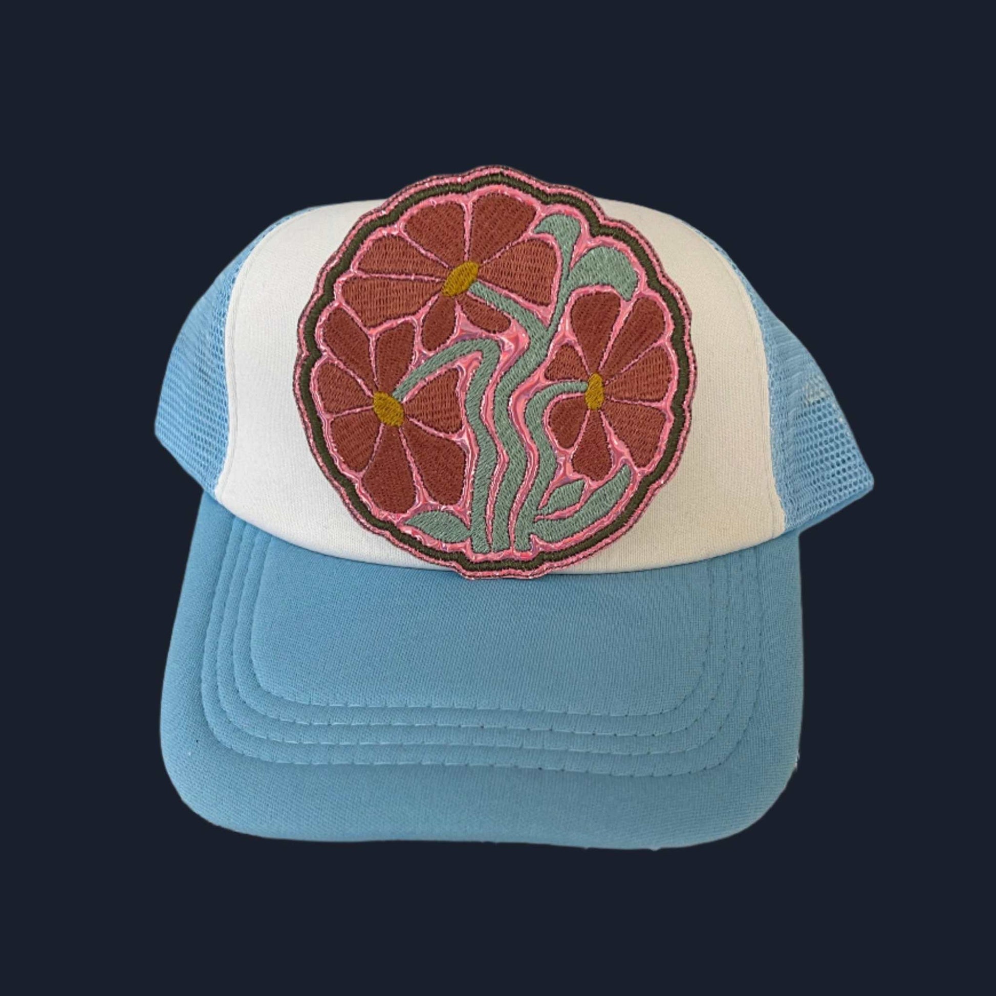 Iron-on patch featuring three muted pink flowers with yellow centers, connected by teal green stems and outlined in dark pink thread.