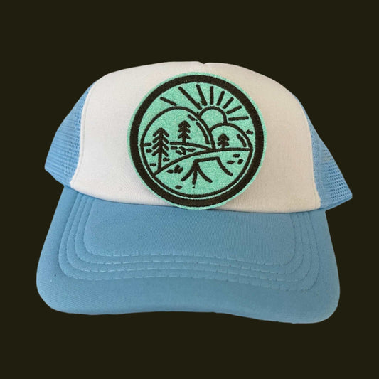 Iron-on patch featuring a serene outdoor scene with a winding river, tall trees, and a setting sun, embroidered in black on a mint green background with a black outline.