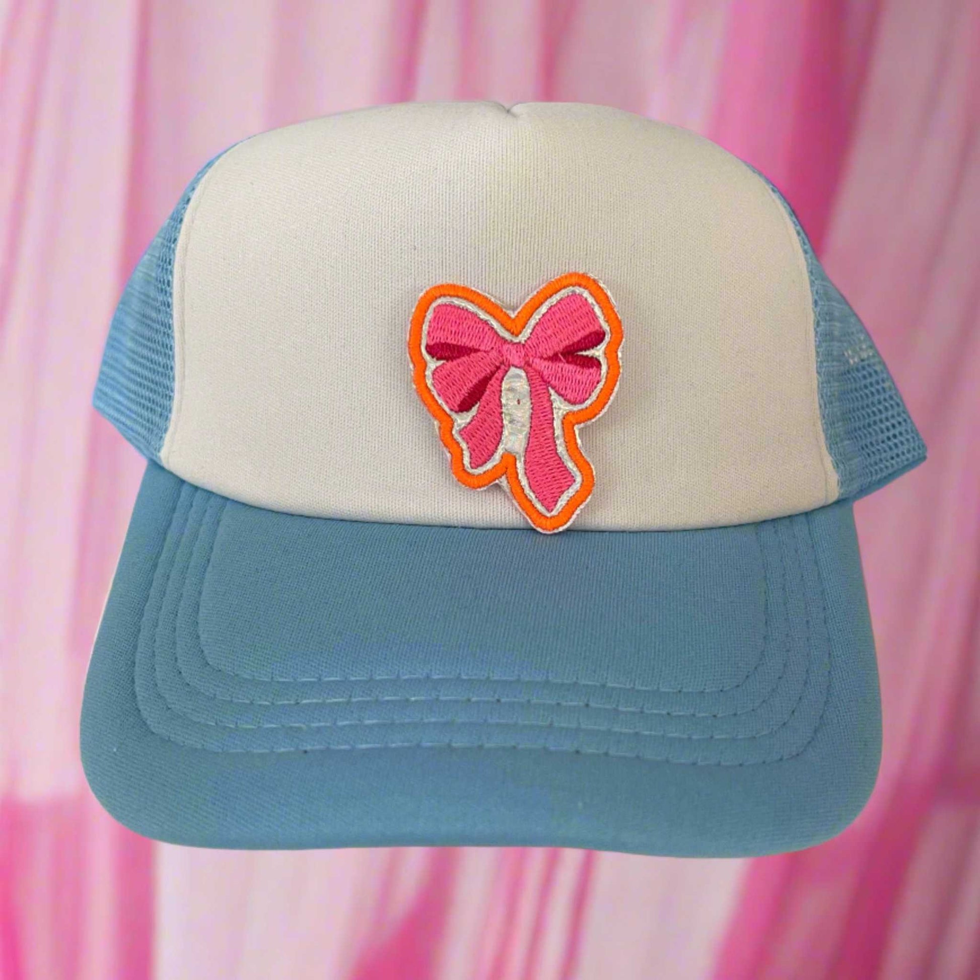 Close-up of a pink ribbon bow embroidered patch with orange and pink detailing, perfect for customizing hats and other accessories.