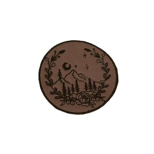 Mountain scene embroidered patch with rustic design, featuring mountains, trees, and floral border.
