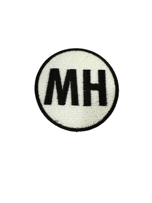 MH BLACK embroidered patch on white background.