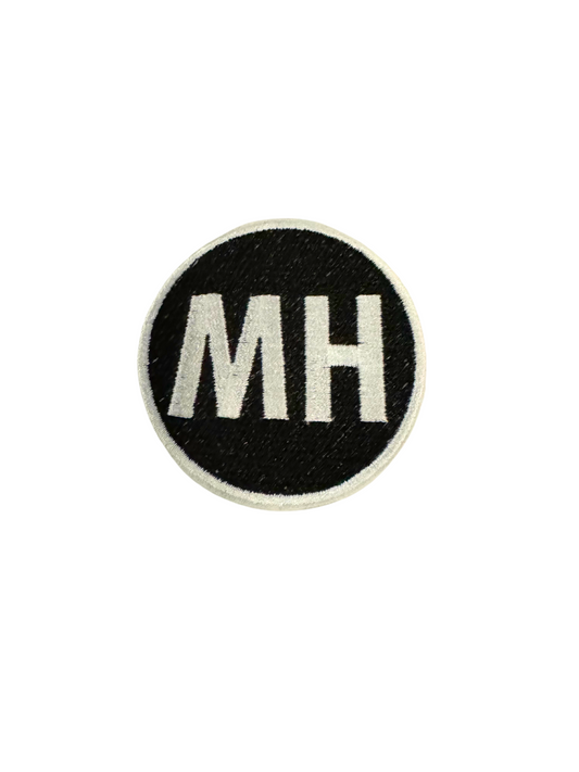 MH WHITE ON BLACK circular patch with white lettering on a black background.