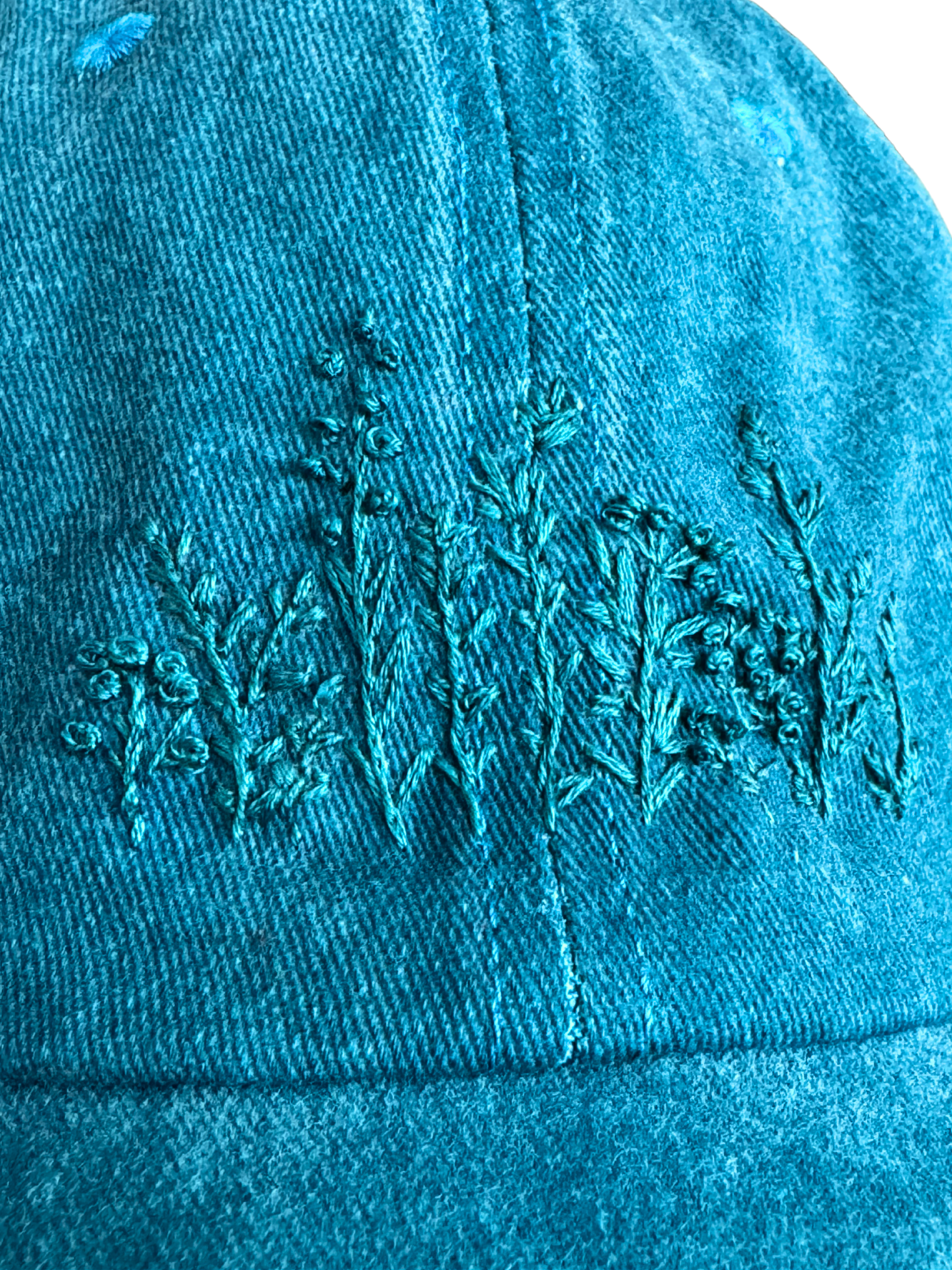 Hand-embroidered wildflower design in teal thread on a teal hat.

