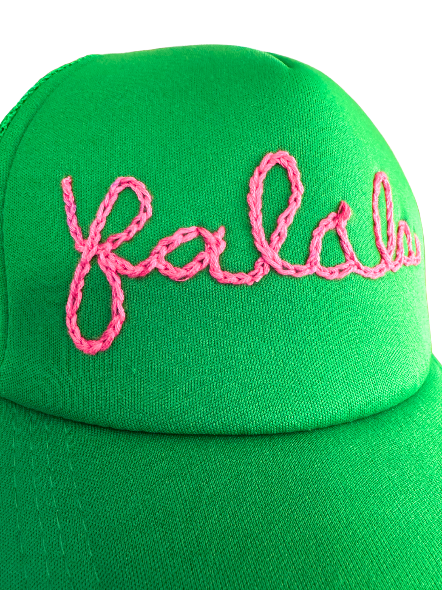 Bright green hat with "Fa La La" pink embroidery in playful cursive.
