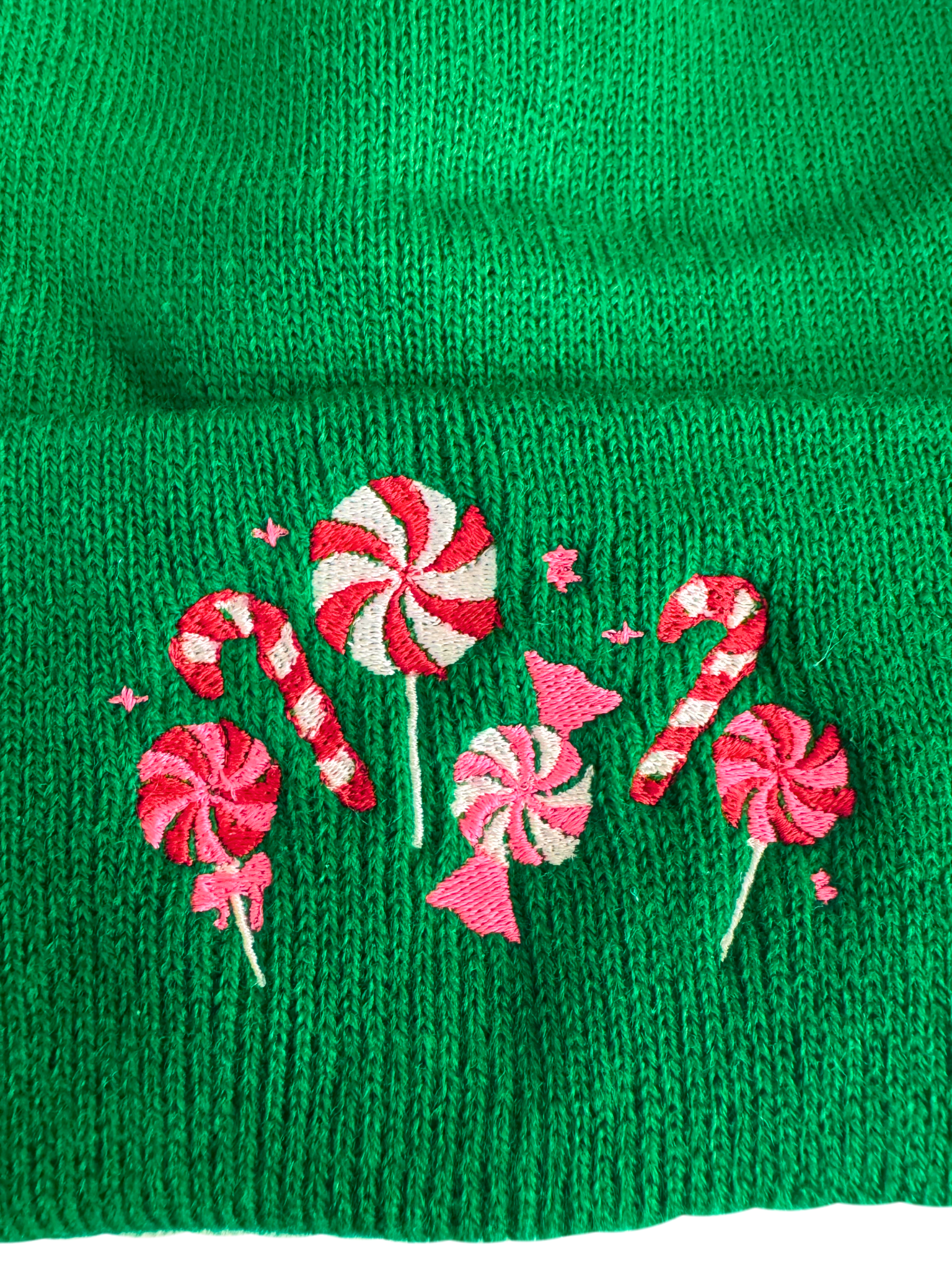 Green beanie with candy cane and peppermint embroidery in red, pink, and white, showcasing festive holiday designs.

