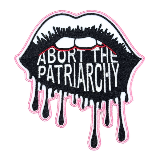 Close-up of an embroidered "Abort the Patriarchy" patch featuring dripping black lips and bold white lettering.
