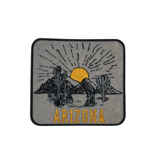 "Embroidered patch featuring an Arizona desert scene with cacti, mountains, and a golden sunset on a neutral gray background."
