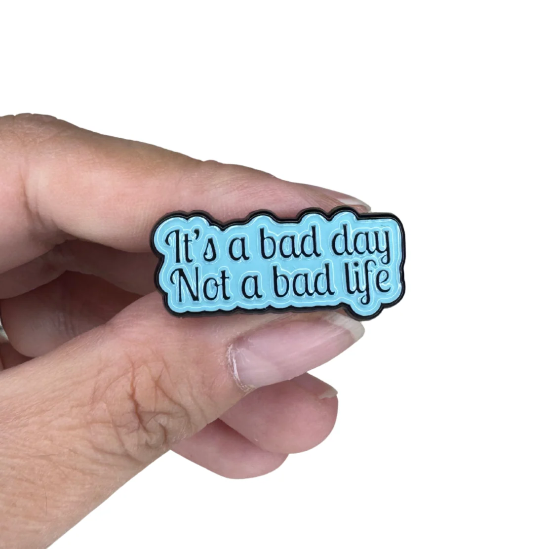 It's a Bad Day Not a Bad Life enamel pin held in hand for scale