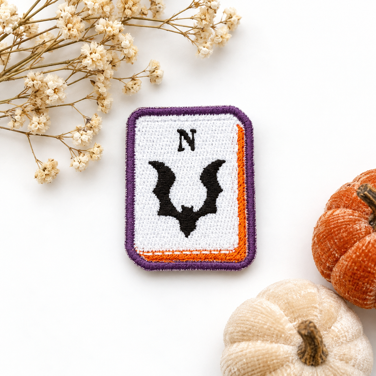 Bat North mahjong tile embroidered patch with purple border and orange accents on white studio background