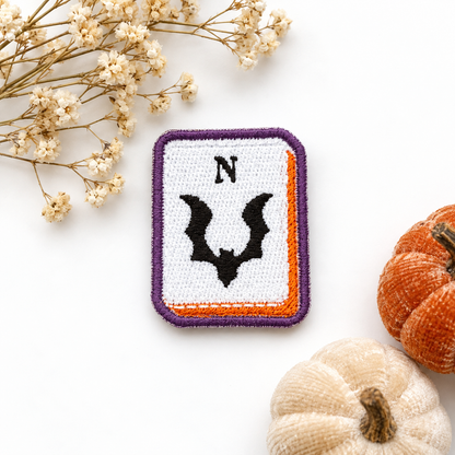 Bat North mahjong tile embroidered patch with purple border and orange accents on white studio background