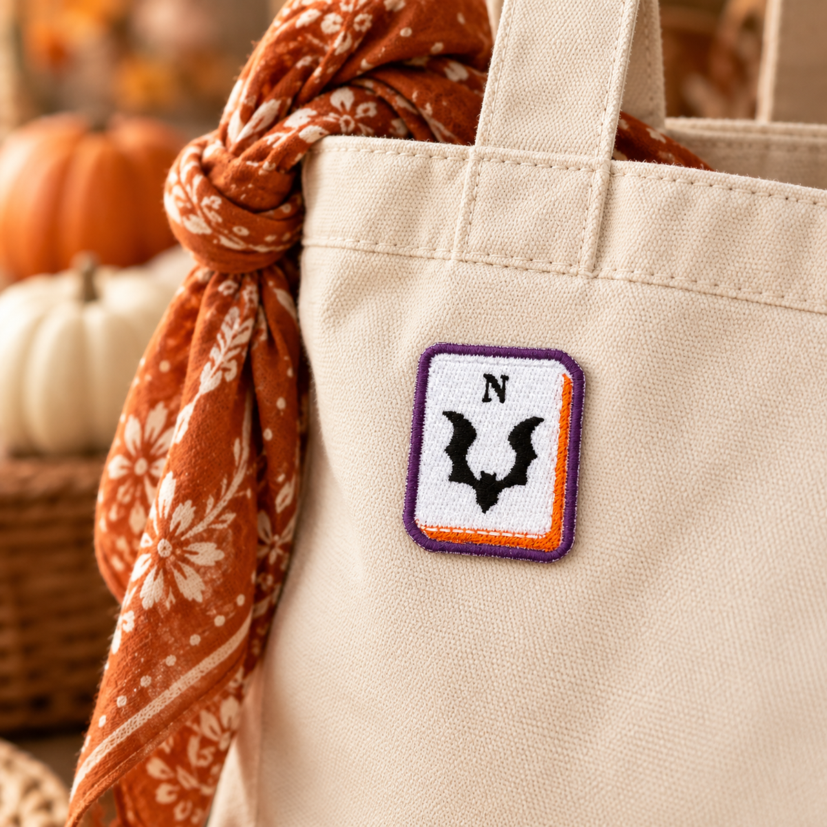 Bat North mahjong embroidered patch displayed on cream canvas tote with rust floral scarf