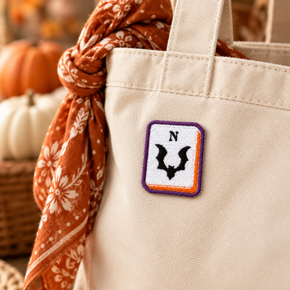 Bat North mahjong embroidered patch displayed on cream canvas tote with rust floral scarf