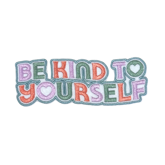 Close-up of an embroidered "Be Kind to Yourself" patch in pastel colors.
