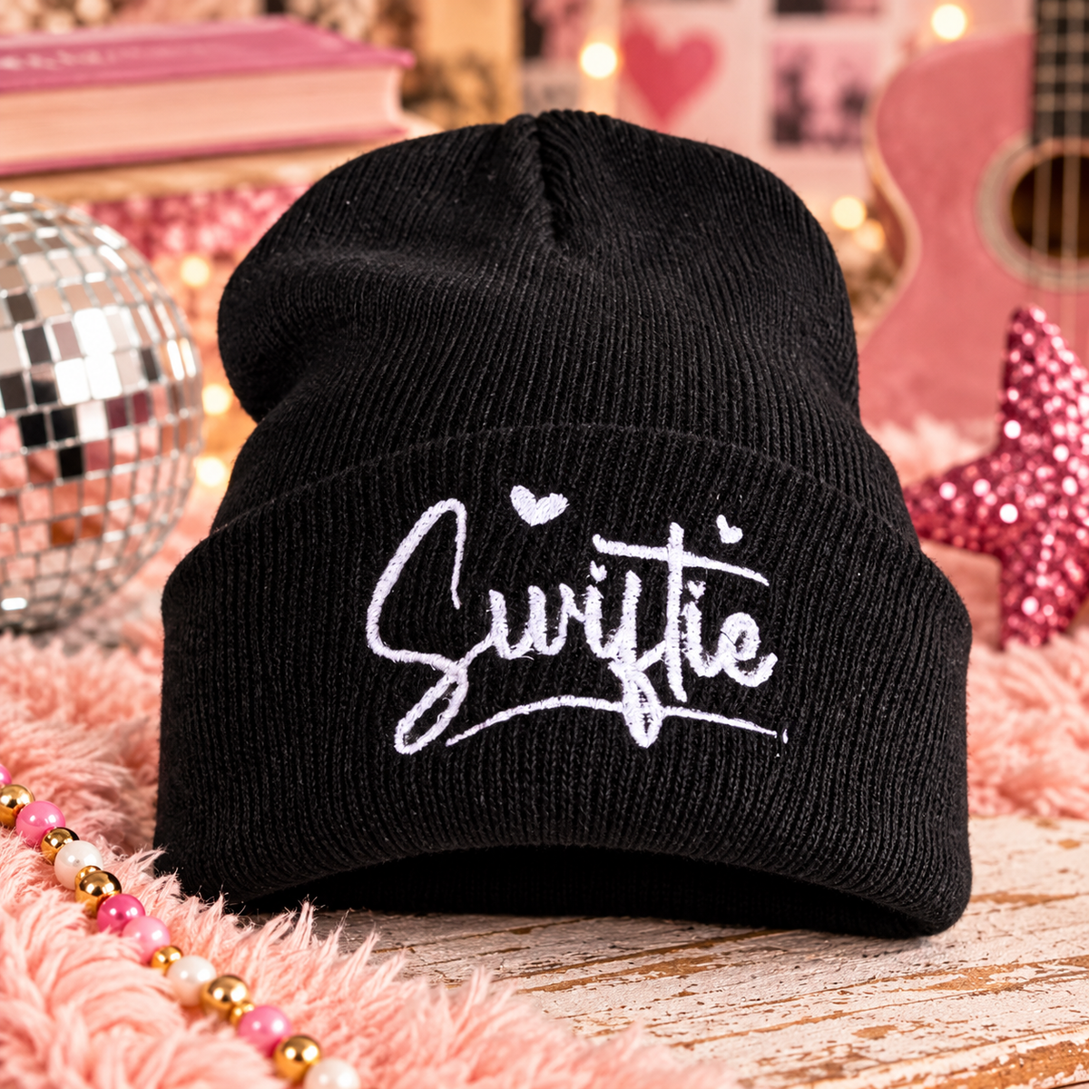 Black Swiftie embroidered youth beanie with white script and heart details in a playful music-inspired setting.