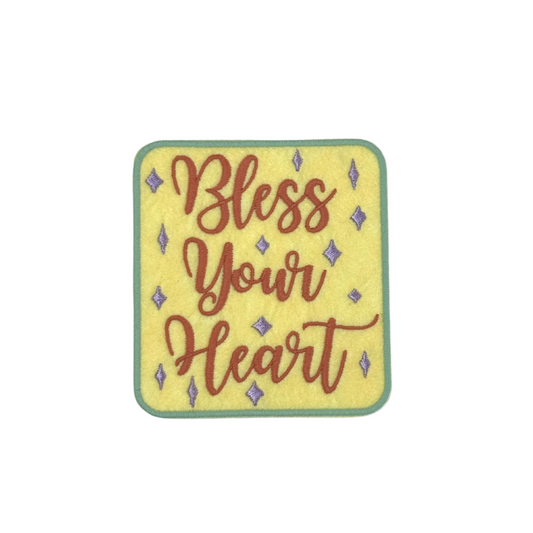 "Square embroidered patch with 'Bless Your Heart' in retro-style script on a yellow background with decorative sparkles."
