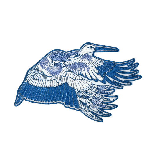 Close-up of a blue heron embroidered patch with intricate floral detailing.

