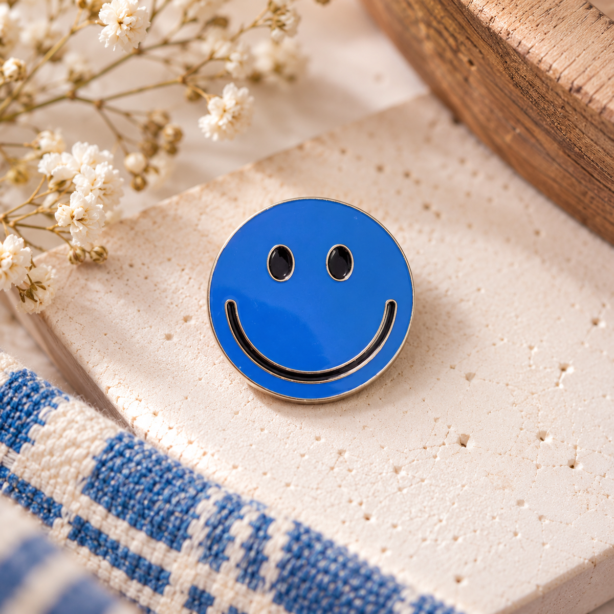 Blue smiley face enamel pin with black eyes and smile, silver-tone outline, styled product hero
