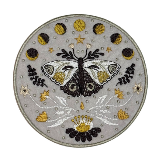 Embroidered moth patch with moon phases, gold stars, and flowers on a gray background
