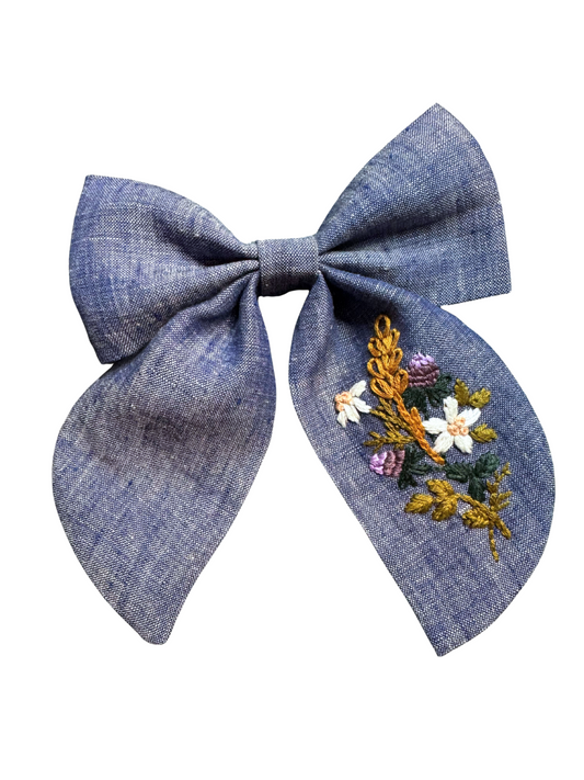 Chambray blue linen bow with hand embroidered floral bouquet, attached to an alligator clip.