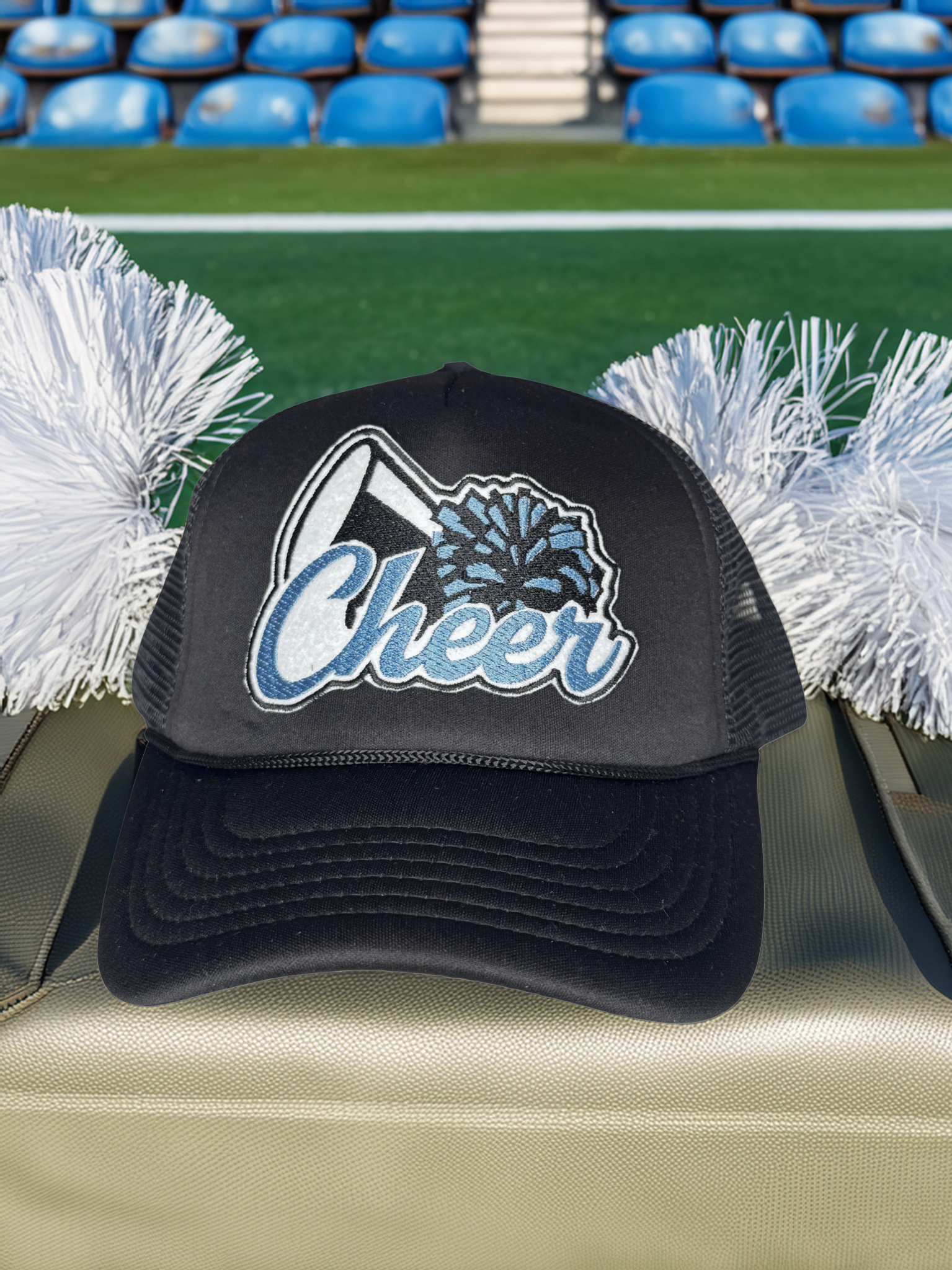 Black cap with 'Cheer' text and pom-poms on a stadium bench