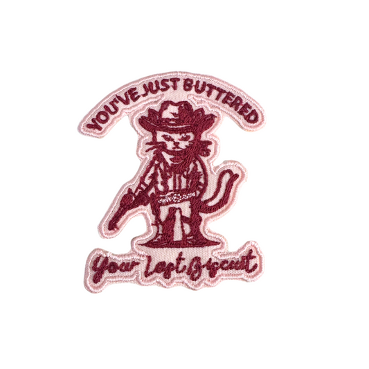 Handmade "You’ve Just Buttered Your Last Biscuit" cowboy cat embroidered patch in burgundy and blush tones.
