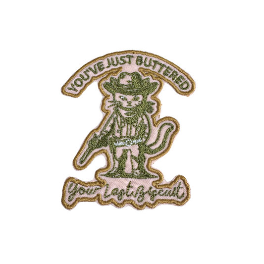 Handmade "You’ve Just Buttered Your Last Biscuit" embroidered patch featuring green and gold tones with a cowboy cat design.
