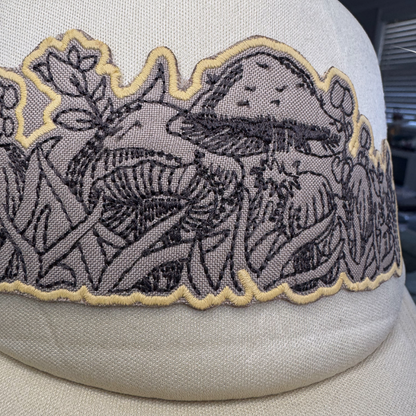Closeup of scalloped black and gold mushroom embroidery on neutral foam-front trucker hat