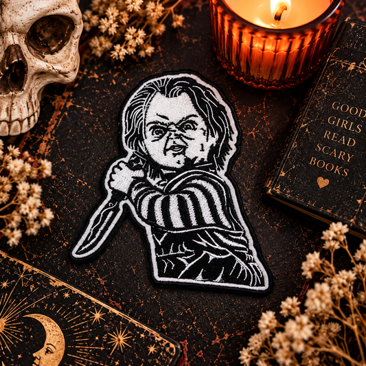 Creepy Killer Doll embroidered iron-on patch styled in a moody Halloween flat lay