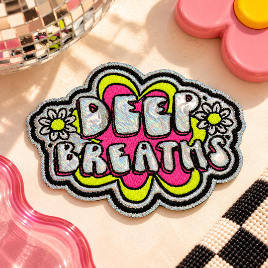 Deep Breaths embroidered iron-on patch with silver holographic letters, neon pink and yellow-green design, and daisies on retro cream flat lay