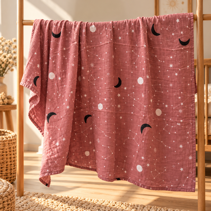 Dusty rose celestial cotton gauze swaddle shown full size on a wooden nursery rack