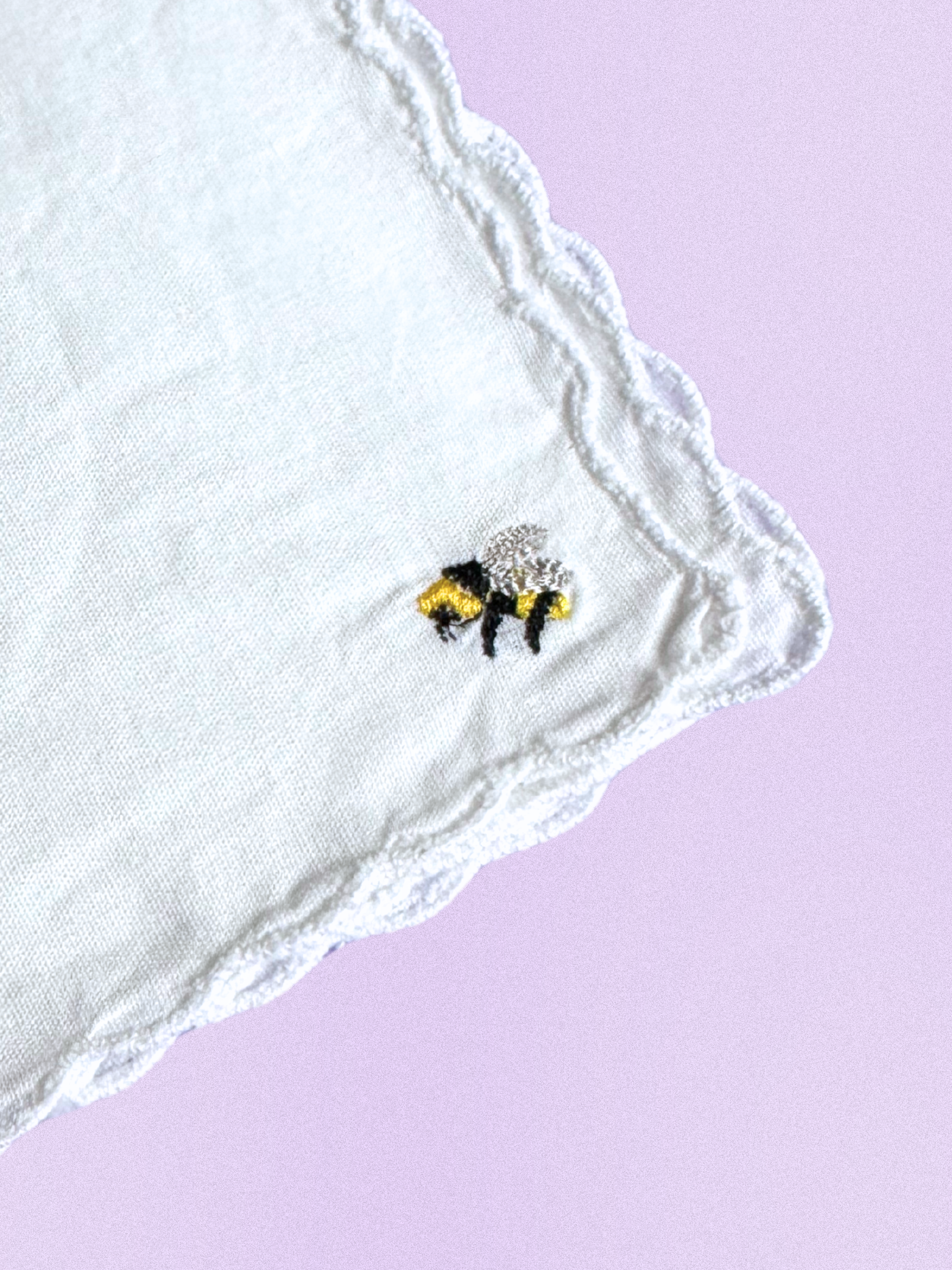A white cotton handkerchief featuring an embroidered bumblebee in black, gold, and silver threads, finished with scalloped edges.
