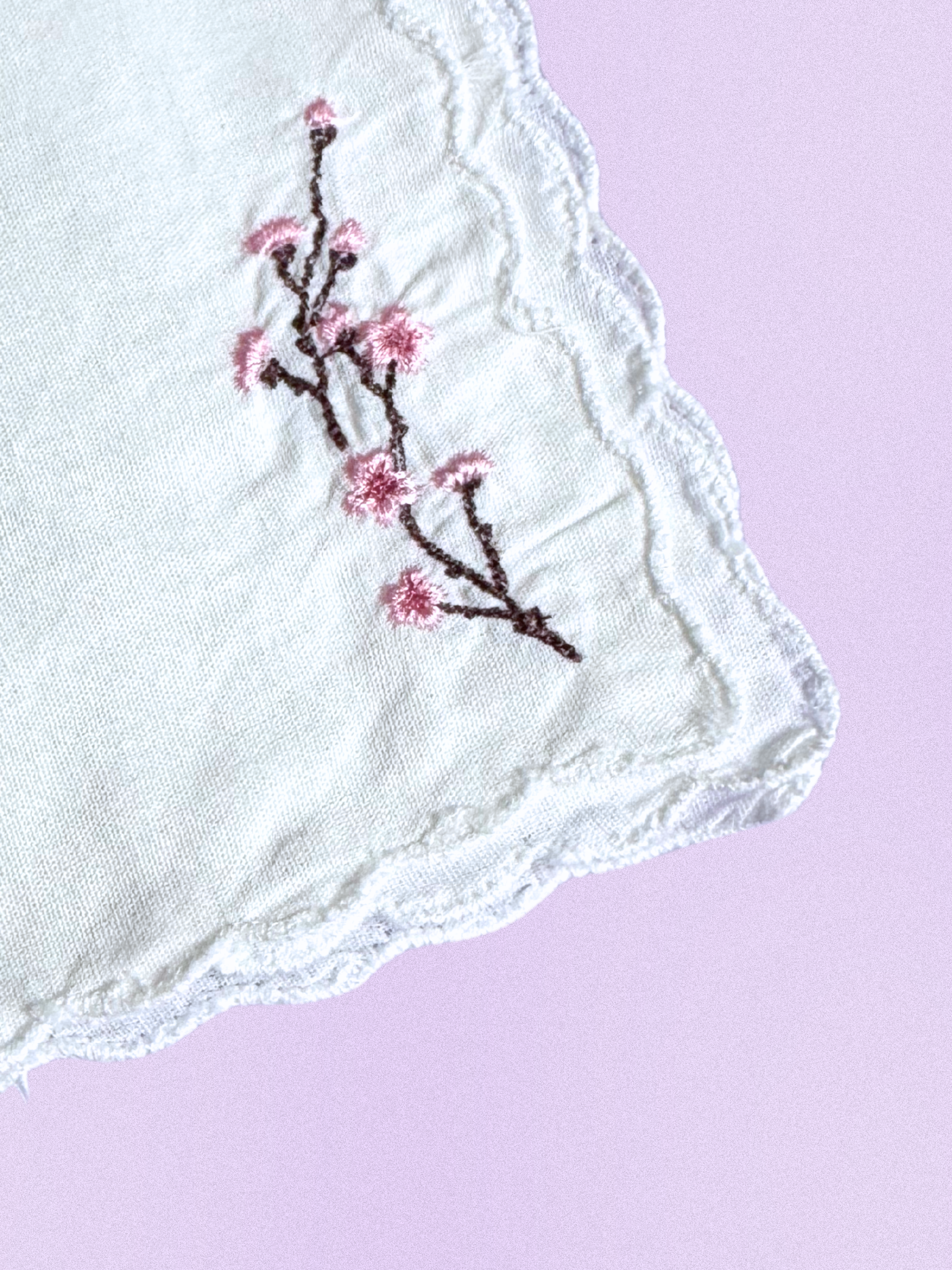 A white cotton handkerchief featuring an embroidered cherry blossom branch with soft pink flowers and brown stems, finished with scalloped edges.

