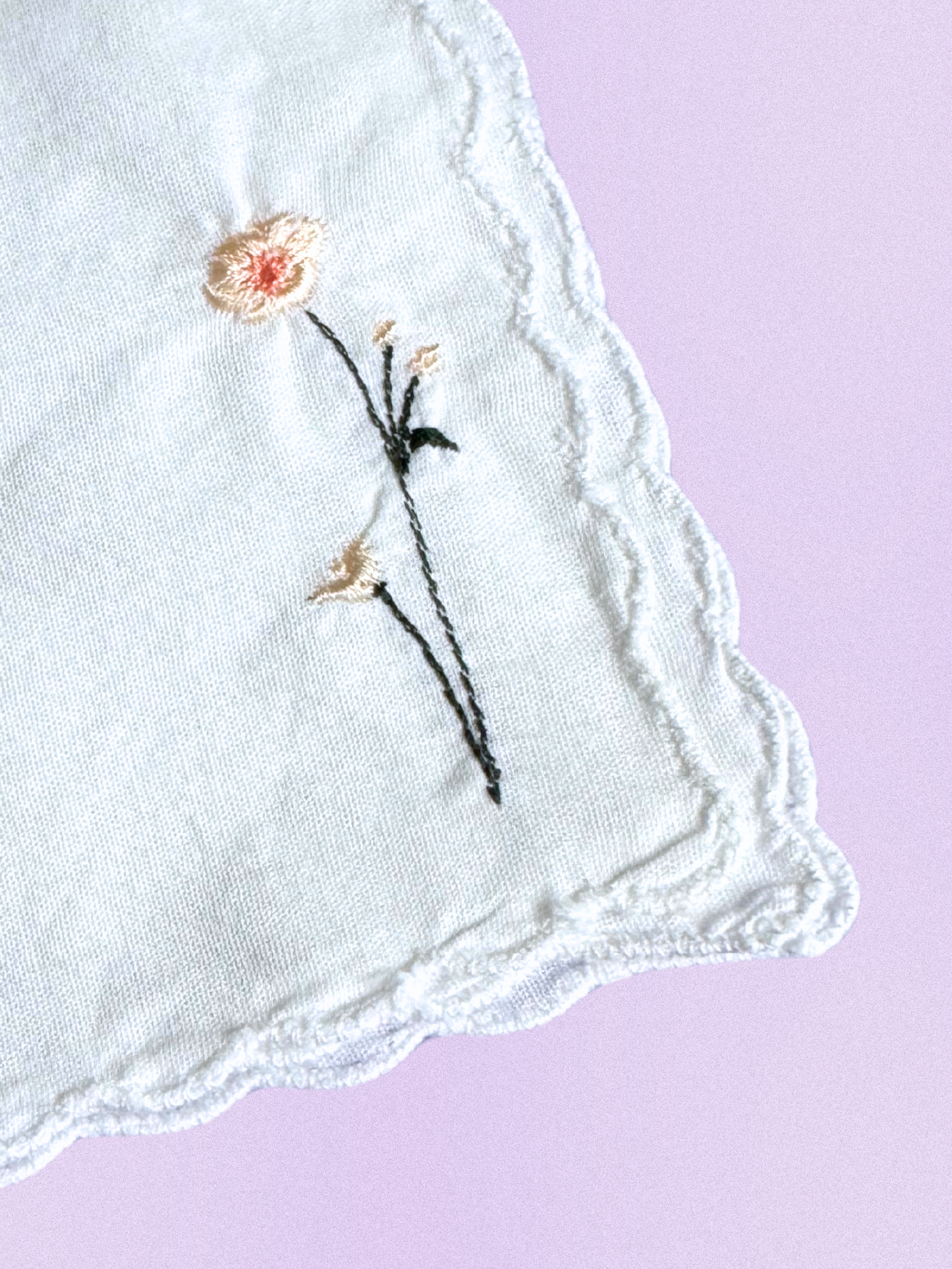 A white cotton handkerchief featuring an embroidered daisy design in soft cream and peach, finished with delicate scalloped edges.
