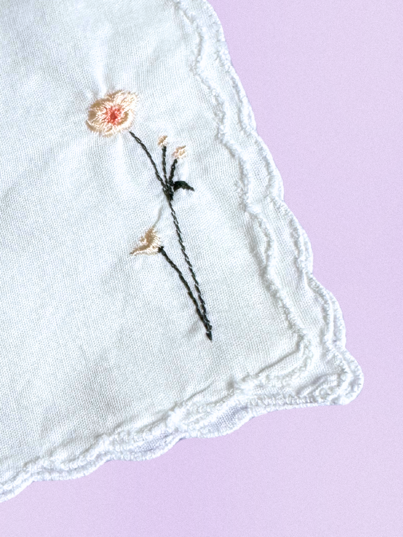A white cotton handkerchief featuring an embroidered daisy design in soft cream and peach, finished with delicate scalloped edges.
