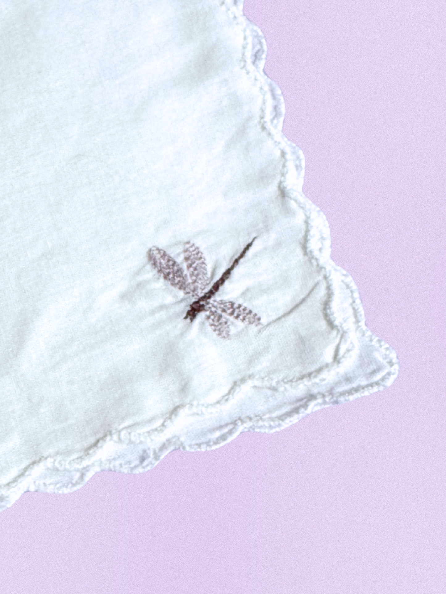 A white cotton handkerchief featuring an embroidered dragonfly in soft taupe, finished with scalloped edges.
