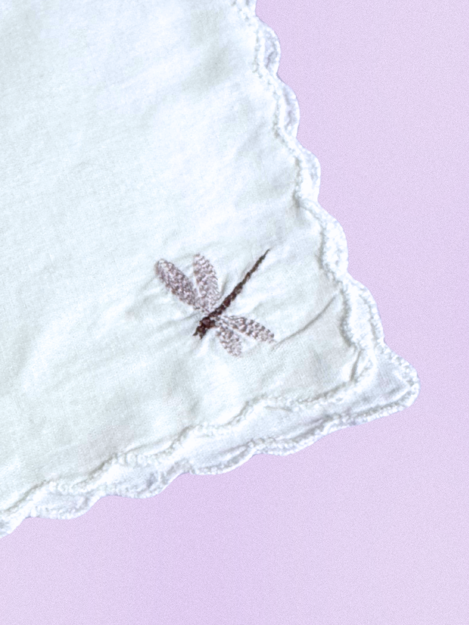 A white cotton handkerchief featuring an embroidered dragonfly in soft taupe, finished with scalloped edges.
