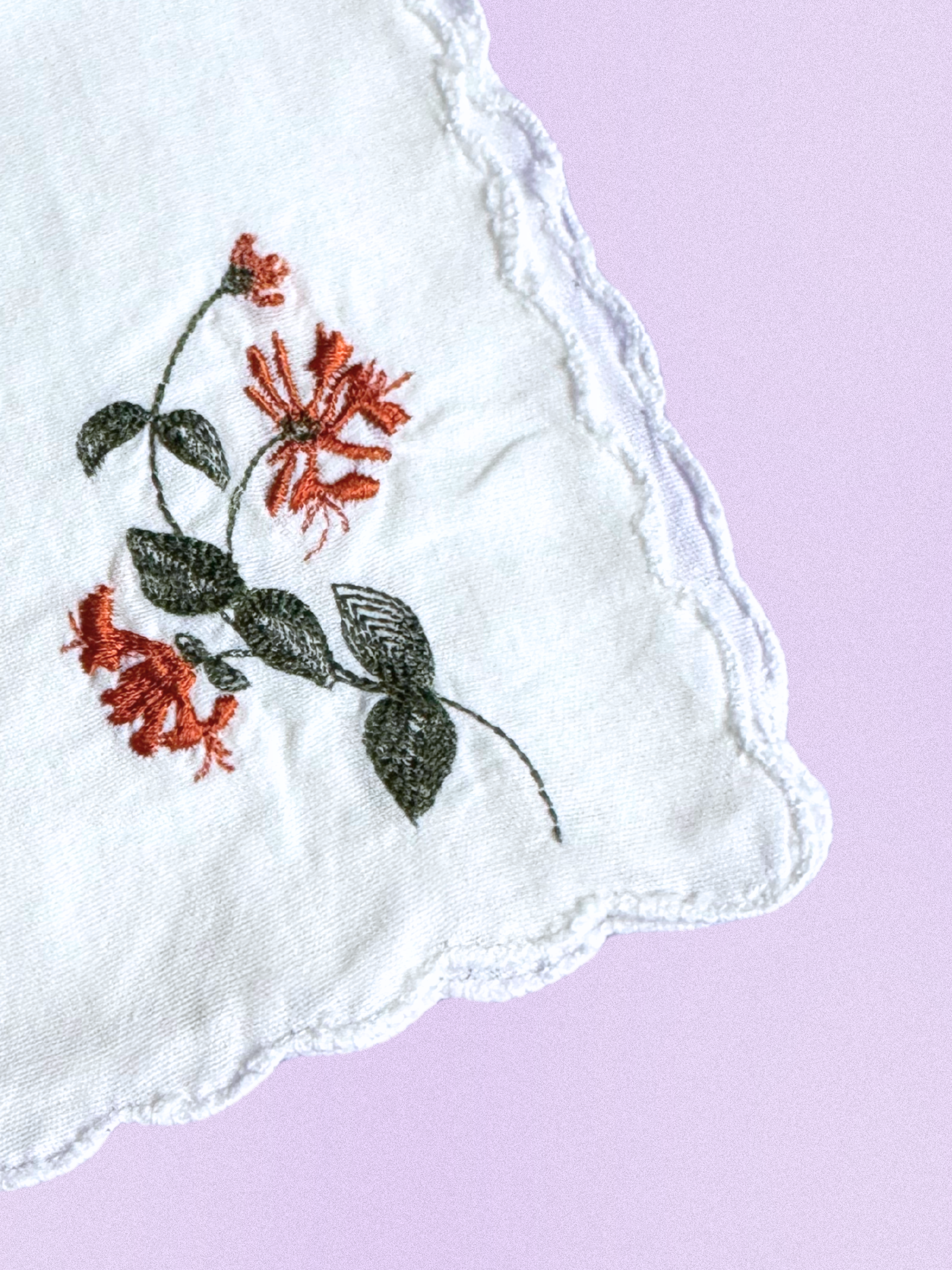 A white cotton handkerchief featuring an embroidered honeysuckle floral design in warm rust and green, finished with scalloped edges.
