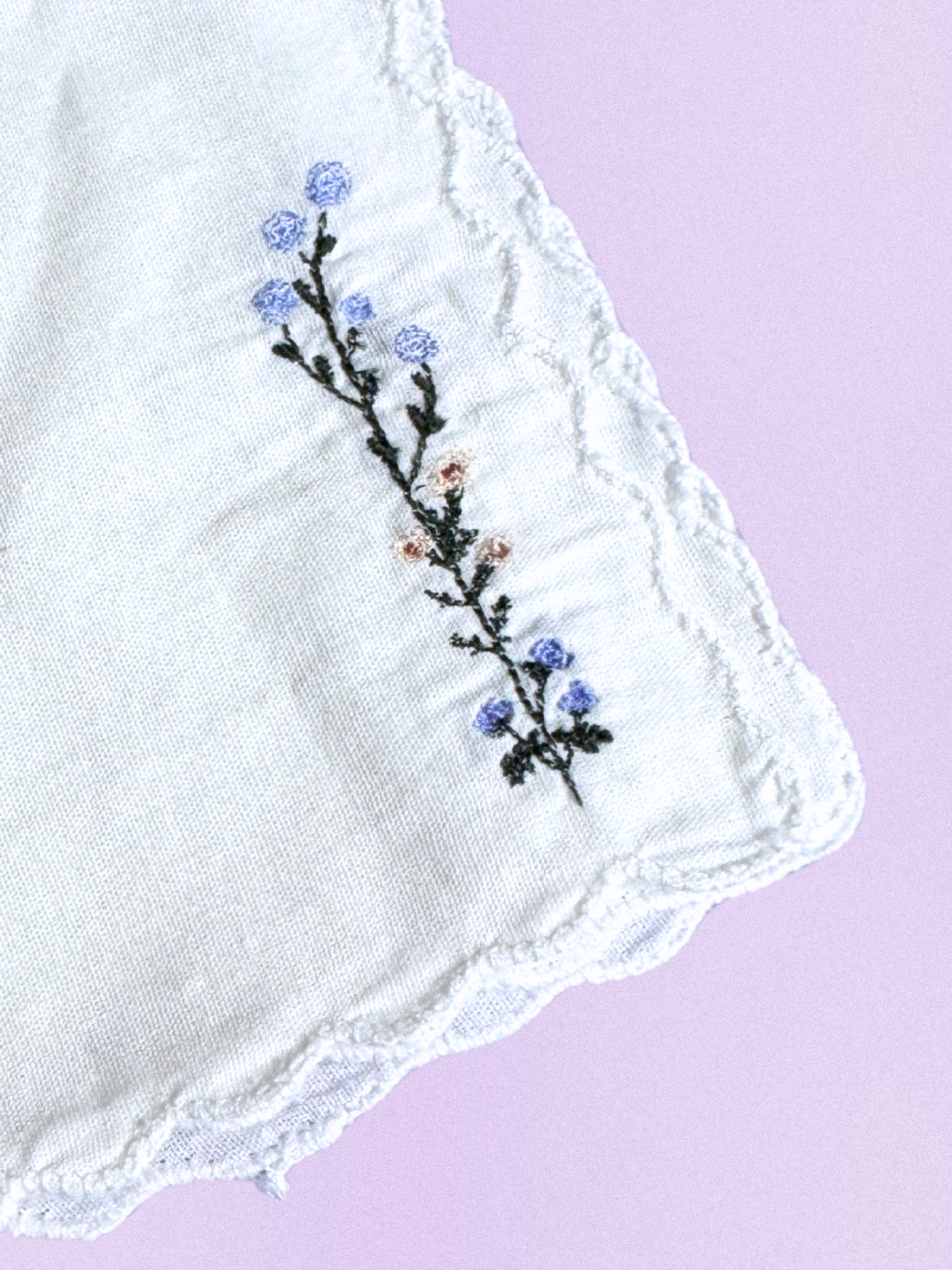 A white cotton handkerchief featuring an embroidered wildflower design with soft blue and peach blossoms, finished with scalloped edges.

