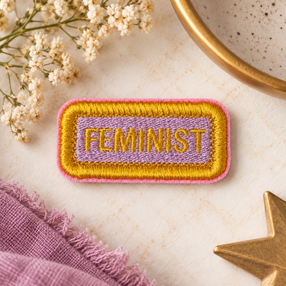 FEMINIST gold and lavender embroidered name tag patch with pink edge on warm vintage flat lay